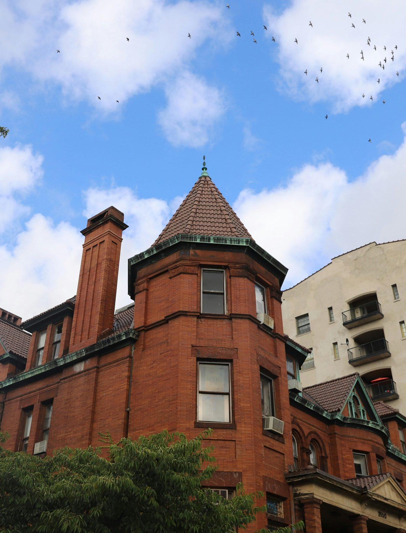 Red-brick building with a corner turret and slate roof against a blue sky